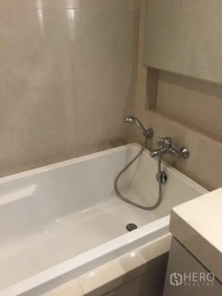 公寓 出租在Watthana, Bangkok - 浴室设嵌入式浴缸与手持花洒，浅色石材墙面。