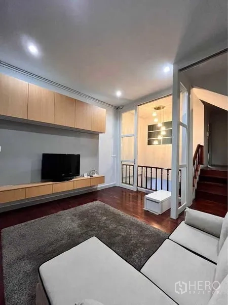 ทาวน์เฮาส์ ให้เช่าในKhlong Toei, Bangkok - ห้องพักผ่อนพร้อมชุดวางทีวี โซฟา พรม และผนังกระจกกั้นบันได