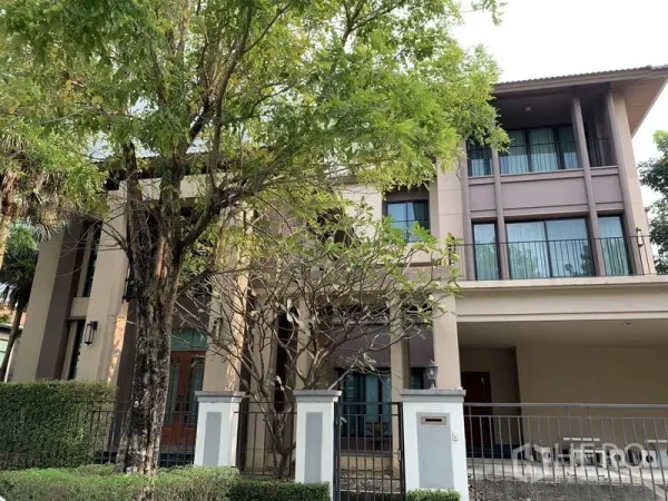 Detached House for rent or sale in Khan Na Yao, Bangkok - Front elevation of luxury detached house behind fence shaded by trees.
