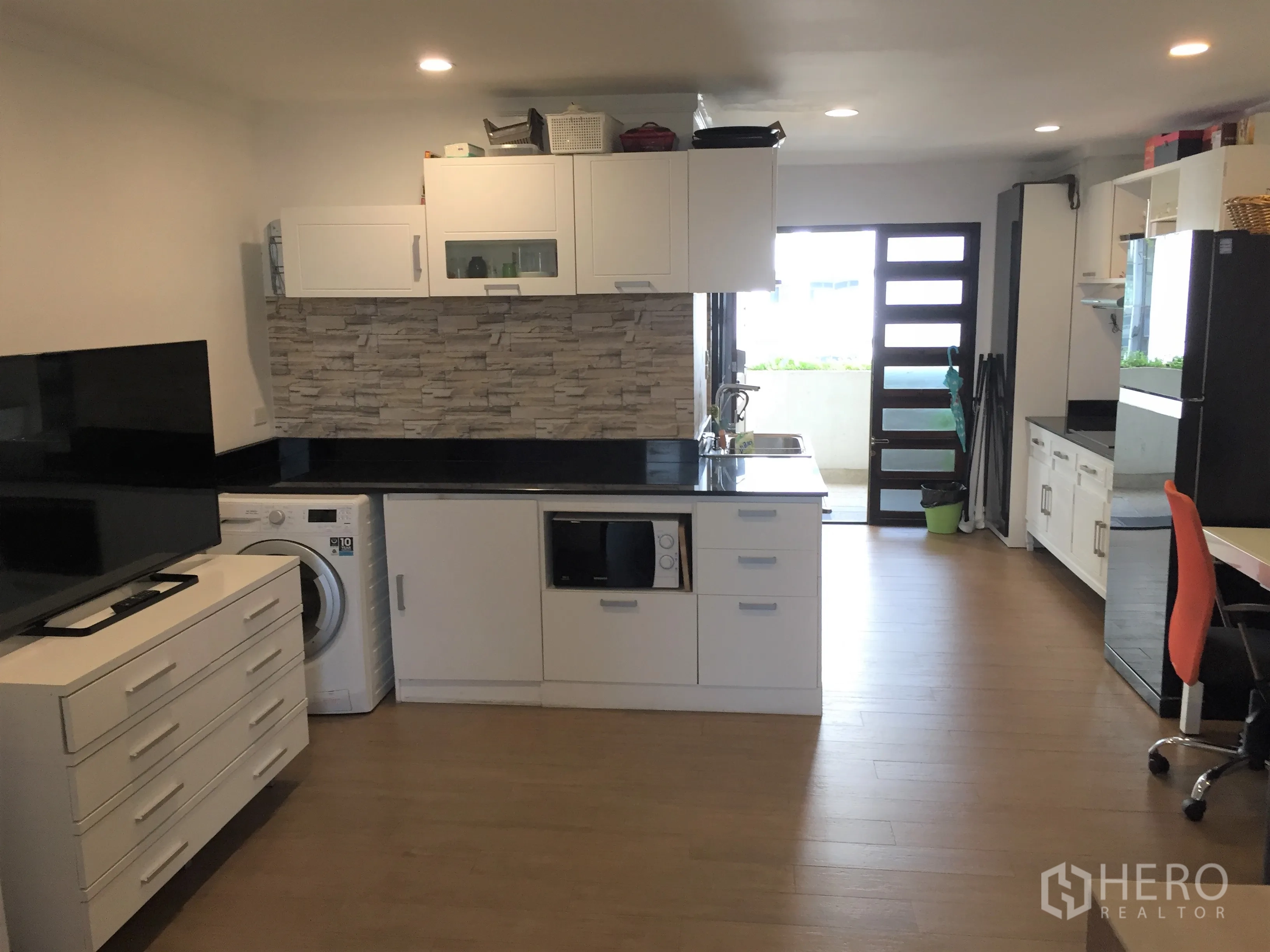 公寓 出租在Watthana, Bangkok - 现代白色厨房，石纹挡板与黑色台面，配洗衣机和微波炉，通往阳台。