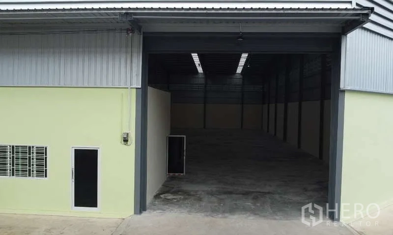 货栈 出租在Ban Phaeo, Samut Sakhon - 仓库外立面，配宽幅卷闸门、行人门和通风窗。