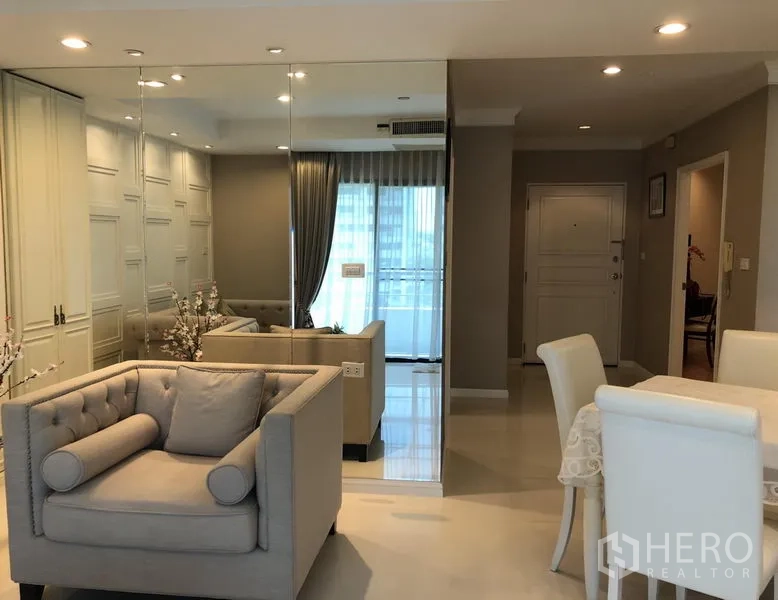 公寓 出租或出售在Sathon, Bangkok - 半开放起居区，落地镜、单人沙发、餐桌与通向阳台的门。