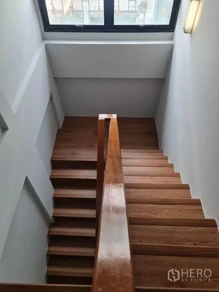 Townhouse for sale in Suan Luang, Bangkok - Wooden staircase with handrail leading to upper floor beneath a skylight window.