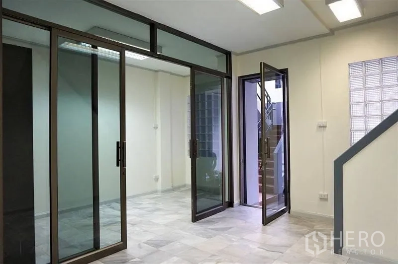 Home Office for rent in Khlong Toei, Bangkok - Open workspace with large sliding glass partitions, marble-look flooring, and door to a small terrace stairwell.