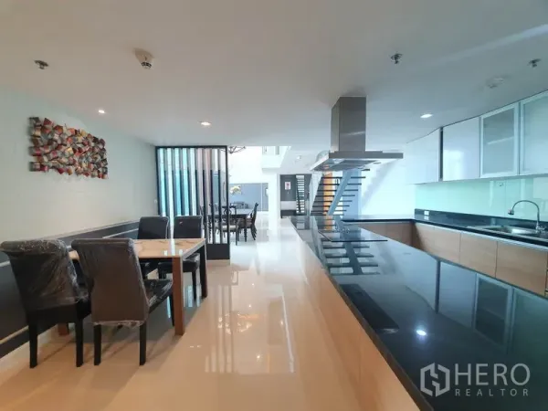 Condominium for rent in Ratchathewi, Bangkok - Open-plan dining and modern kitchen with long black granite countertops, light wood cabinetry, and glossy tile floors.