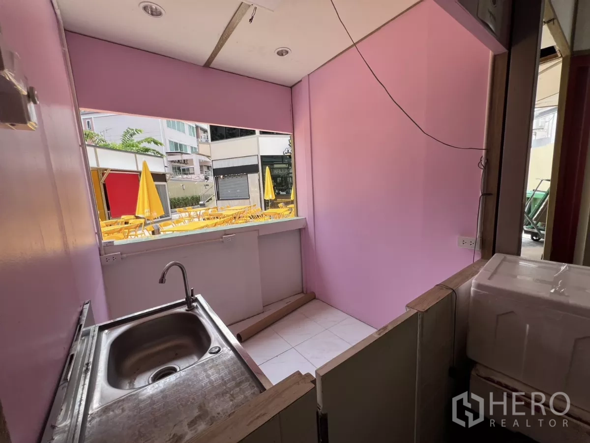 พื้นที่ขายปลีก ให้เช่าในKhlong Toei, Bangkok - เคาน์เตอร์บริการขนาดกะทัดรัดพร้อมอ่างสแตนเลส ผนังสีชมพู มองออกไปยังลานนั่งกลางแจ้งสีเหลือง.
