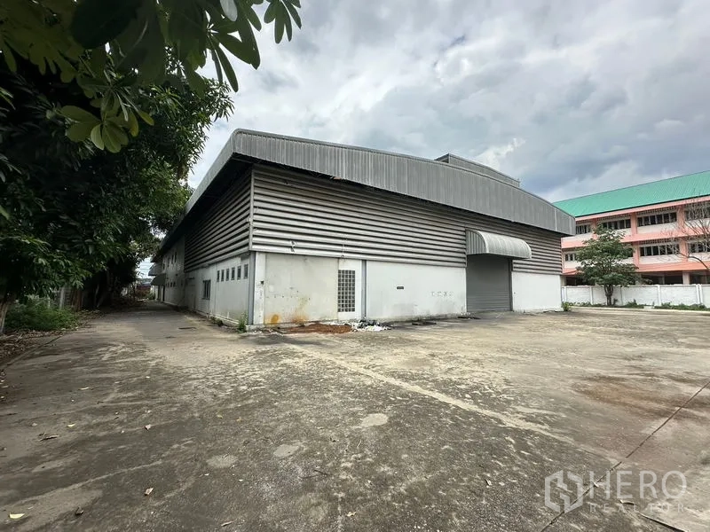 Showroom for rent or sale in Lam Luk Ka, Pathum Thani - Side view of the warehouse with metal cladding and shutters.