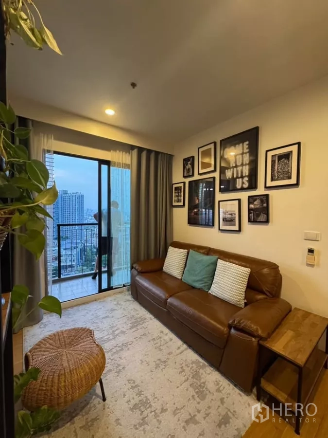 Condominium for rent in Watthana, Bangkok - Living area with gallery wall, curtains and sliding doors to a skyline-view balcony.
