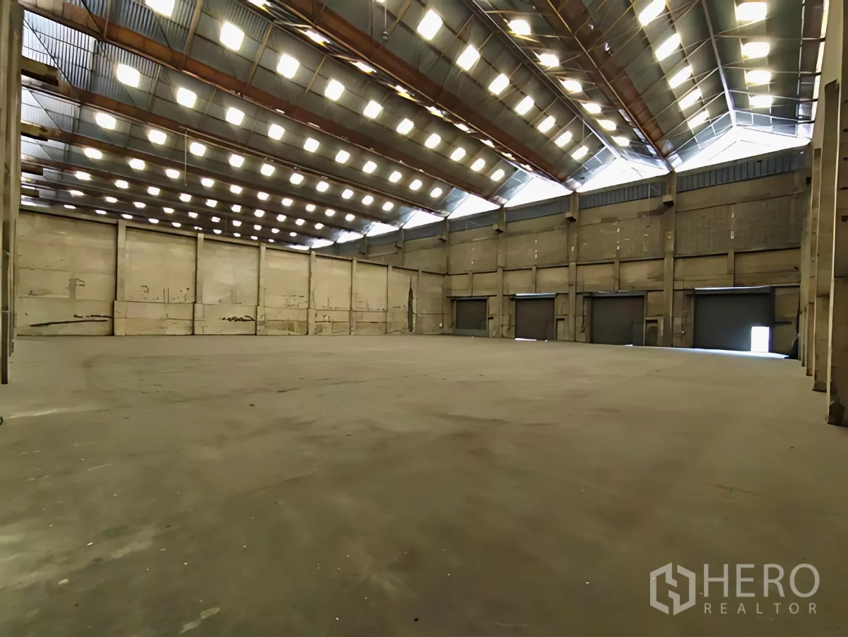 工厂 出租在Khlong Toei, Bangkok - 工厂内部空间开阔，高屋顶采光窗，混凝土地面与多樘卷帘门