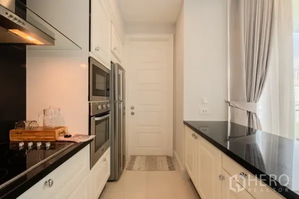 公寓 出售 - 现代走廊式厨房，白色橱柜、黑色台面与嵌入式烤箱