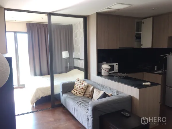 คอนโด ให้เช่าในKhlong Toei, Bangkok - พื้นที่นั่งเล่นแบบโอเพ่นพร้อมโซฟาสีเทา ครัวบิวท์อินท็อปหินสีดำ และห้องนอนกั้นกระจกสไลด์