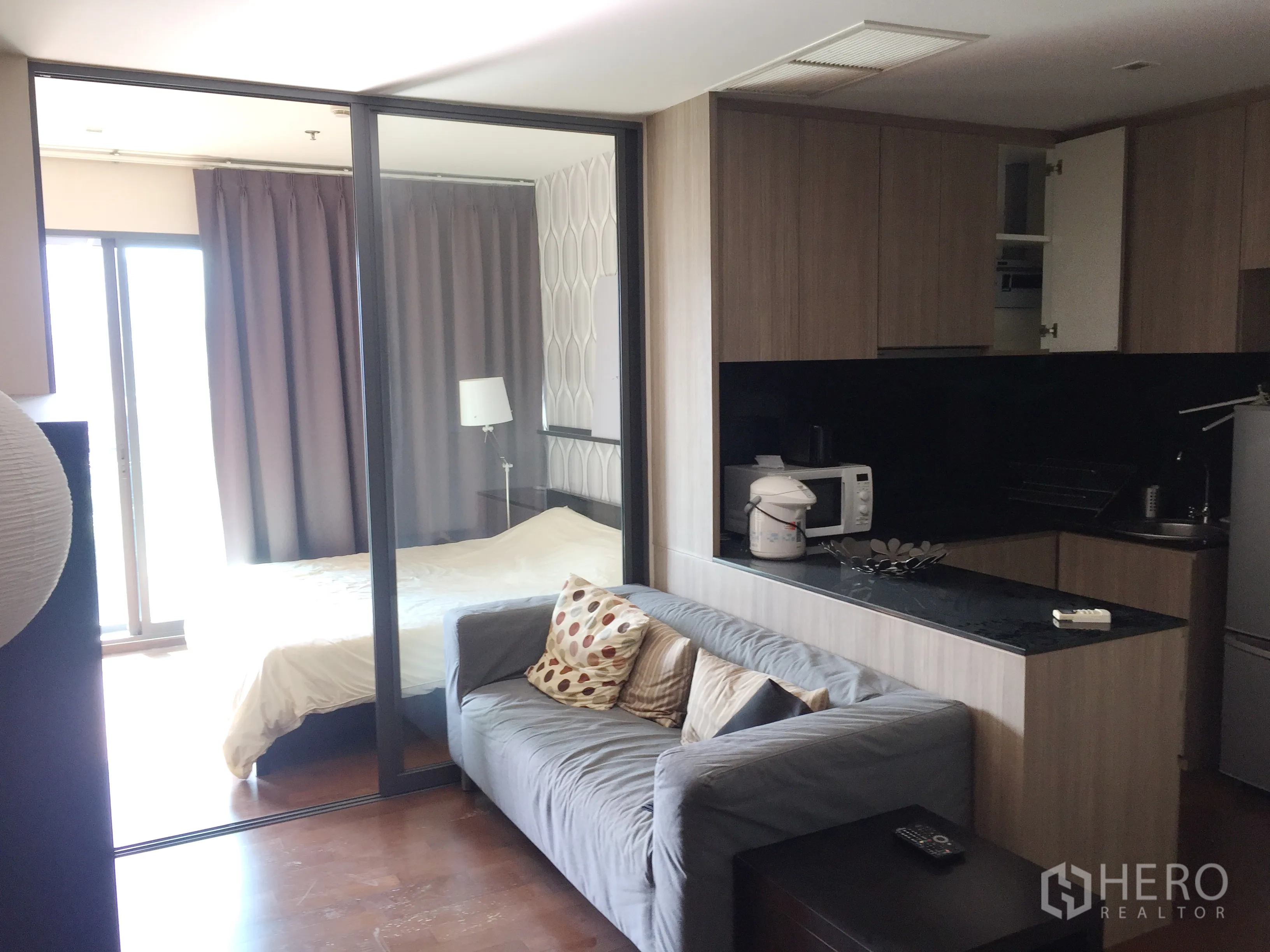 คอนโด ให้เช่าในKhlong Toei, Bangkok - พื้นที่นั่งเล่นแบบโอเพ่นพร้อมโซฟาสีเทา ครัวบิวท์อินท็อปหินสีดำ และห้องนอนกั้นกระจกสไลด์