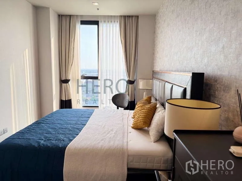 คอนโด ให้เช่า - ห้องนอนมองออกหน้าต่าง เห็นหัวเตียงบุหนังและโต๊ะข้าง