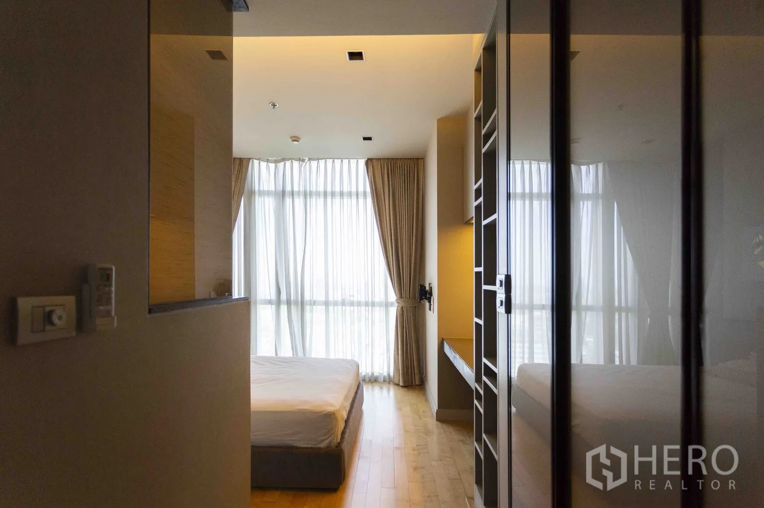Condominium for rent in Pathum Wan, Bangkok - Bright bedroom with tall sheer curtains, floor-to-ceiling windows and built-in storage.