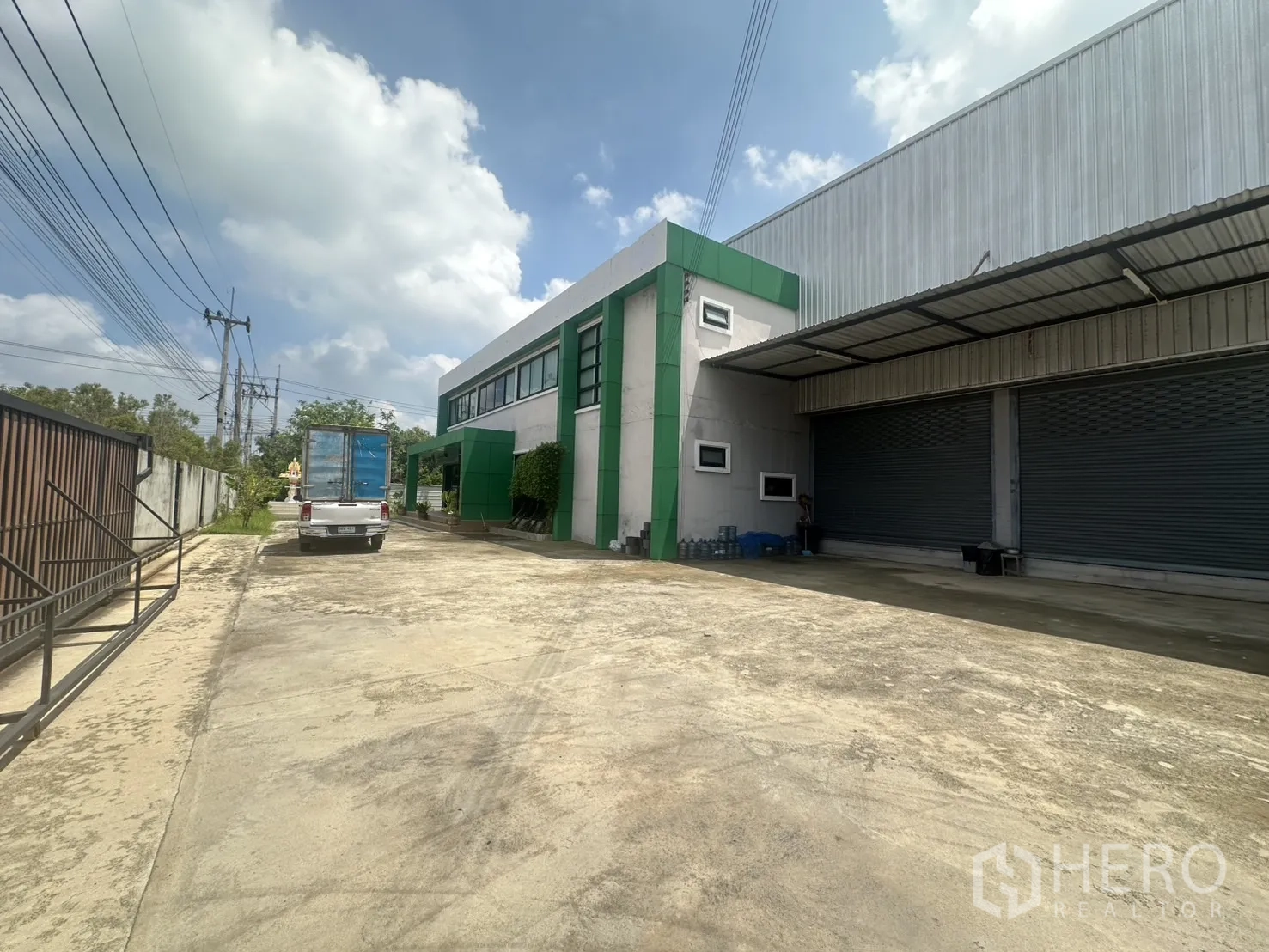Warehouse for sale in Bang Len, Nakhon Pathom - Driveway perspective showing the office facade and covered loading docks.