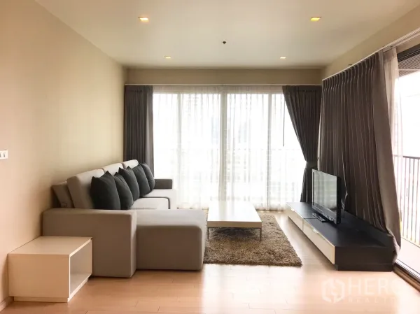 คอนโด ให้เช่าในWatthana, Bangkok - ห้องนั่งเล่นโทนอบอุ่น มีโซฟาเข้ามุม โต๊ะกลาง ตู้วางทีวี และกระจกสูงจรดเพดาน