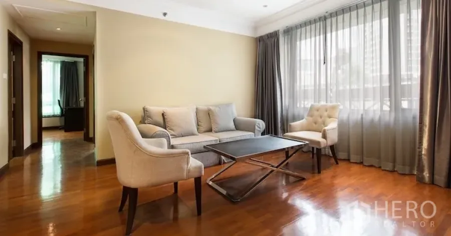 Condominium for rent in Sathon, Bangkok - Bright living room with sofa set, armchairs and a large curtained window over polished wood floors.