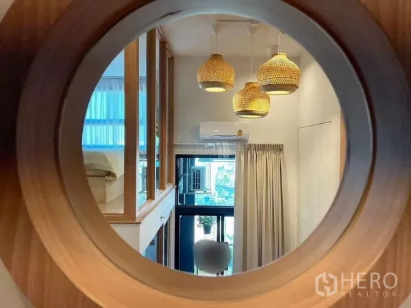 คอนโด ให้เช่าในHuai Khwang, Bangkok - ช่องหน้าต่างวงกลมไม้ มองไปยังห้องนั่งเล่นที่มีโคมหวาย ผ้าม่าน และเครื่องปรับอากาศ