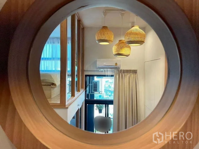 คอนโด ให้เช่าในHuai Khwang, Bangkok - ช่องหน้าต่างวงกลมไม้ มองไปยังห้องนั่งเล่นที่มีโคมหวาย ผ้าม่าน และเครื่องปรับอากาศ