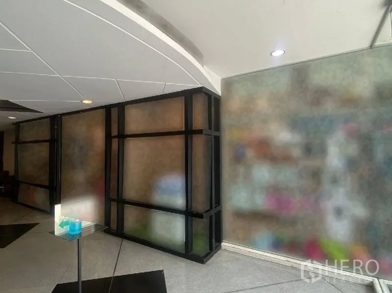 零售空间 出租在Watthana, Bangkok - 室内走廊视角，黑色框架玻璃隔断与弧形白色天花。