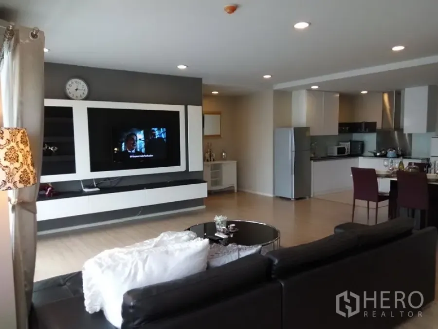 Condominium for rent or sale in Pathum Wan, Bangkok - Open-plan living room with a built-in TV wall, recessed lighting, and a modern kitchen and dining area.