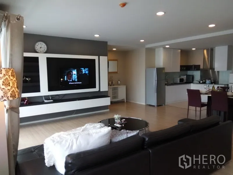 Condominium for rent or sale in Pathum Wan, Bangkok - Open-plan living room with a built-in TV wall, recessed lighting, and a modern kitchen and dining area.