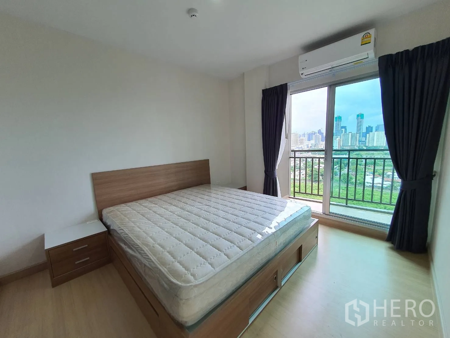 คอนโด for rent in Huai Khwang, Bangkok - ห้องนอนหลัก เตียงควีน โต๊ะข้าง เต้ารับแสงจากประตูกระจกสไลด์ออกระเบียง เห็นวิวเมือง มีแอร์