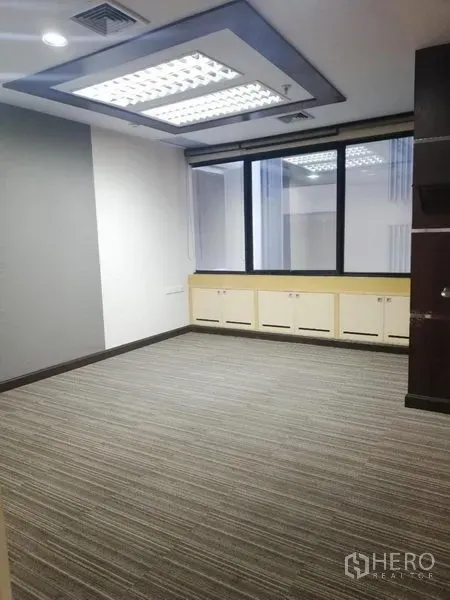 Office Space for rent in Watthana, Bangkok - Private office with grey carpet, fluorescent ceiling lights and a large window with built-in cabinets.