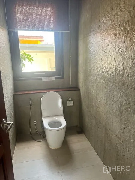 Detached House for sale in Prawet, Bangkok - Compact WC with window, spray hose, and stone-textured walls.