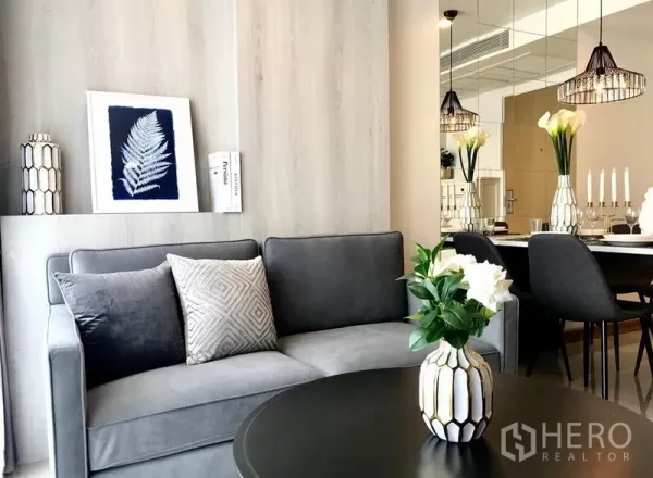 Condominium for rent in Watthana, Bangkok - Contemporary living room with grey sofa, decorative vases, mirror wall and dining area with pendant lights.