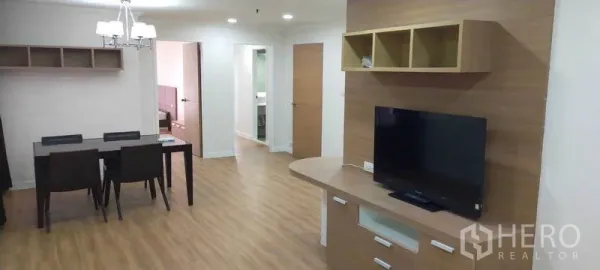 Condominium for rent in Watthana, Bangkok - Open-plan living and dining room with wood flooring, TV console, and table for four.