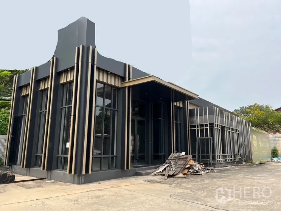 零售空间 出租在Chatuchak, Bangkok - 建筑侧视图与入口，玻璃门面宽阔，前场可供顾客停车。