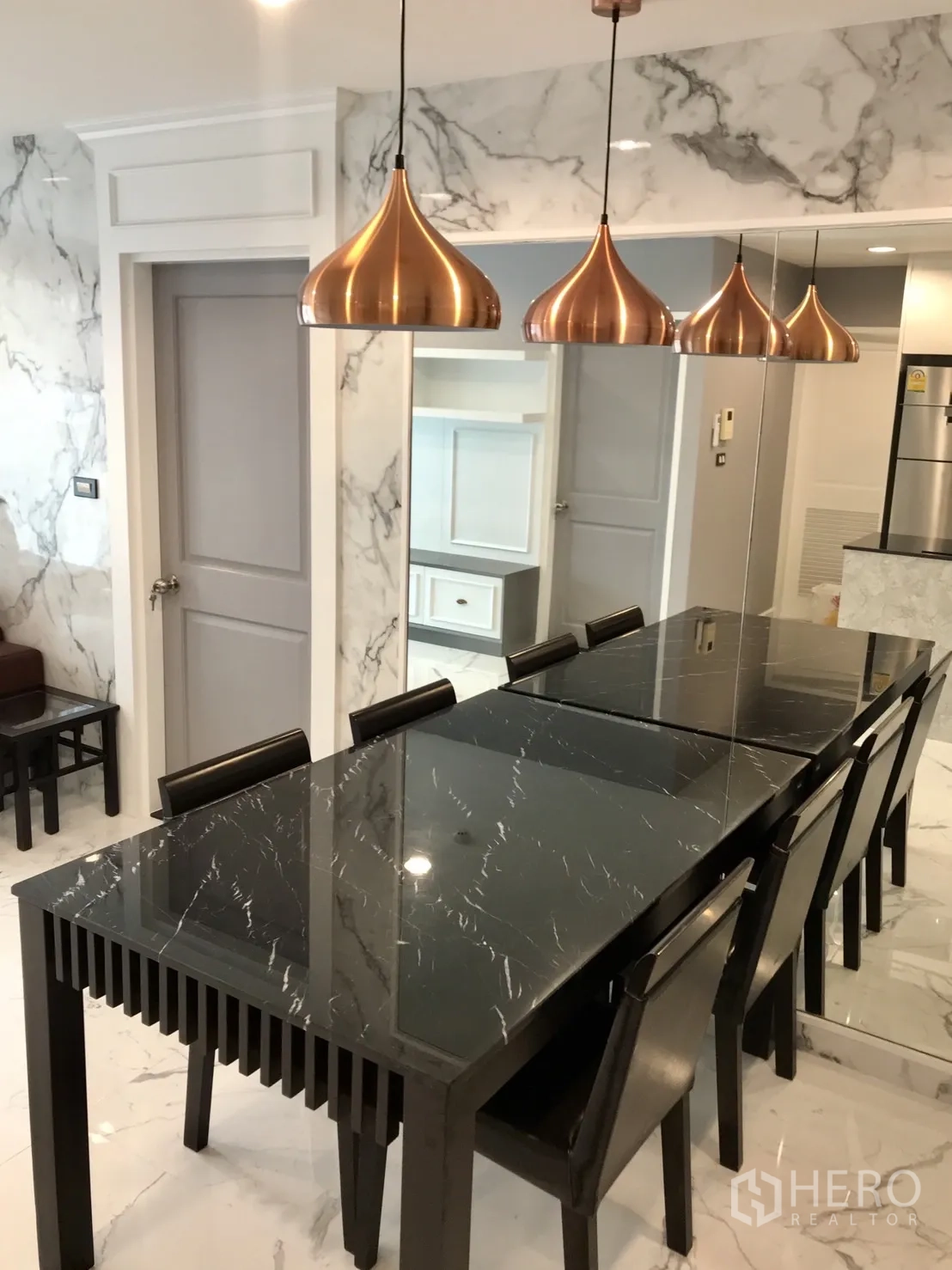 公寓 出租或出售在Khlong Toei, Bangkok - 餐厅设长形黑色玻璃桌、六把椅子和三盏铜色吊灯，旁为镜面墙。