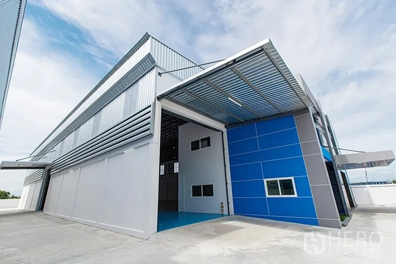 Warehouse for rent in Bang Bo, Samut Prakan - Covered loading bay with large roller shutter and steel canopy on the warehouse side.