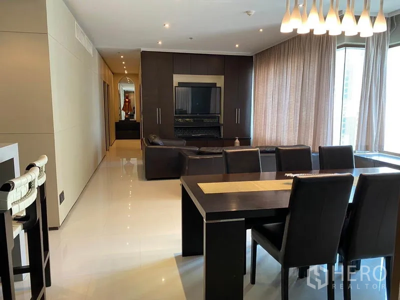 公寓 出租在Khlong Toei, Bangkok - 开放式客餐厅，深色木家具、电视背景墙、吊灯与大窗帘窗户。