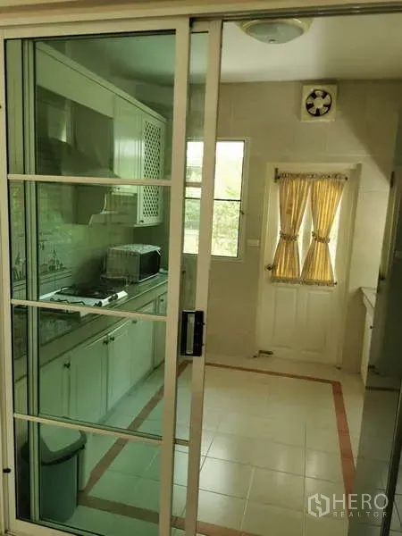 บ้าน ให้เช่า - ครัวปิดหลังประตูกระจกบานเลื่อน ตู้ครัวสีขาว เตา และหน้าต่างผ้าม่านสีเหลือง