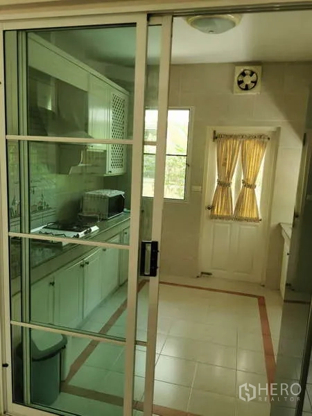 บ้าน ให้เช่า - ครัวปิดหลังประตูกระจกบานเลื่อน ตู้ครัวสีขาว เตา และหน้าต่างผ้าม่านสีเหลือง