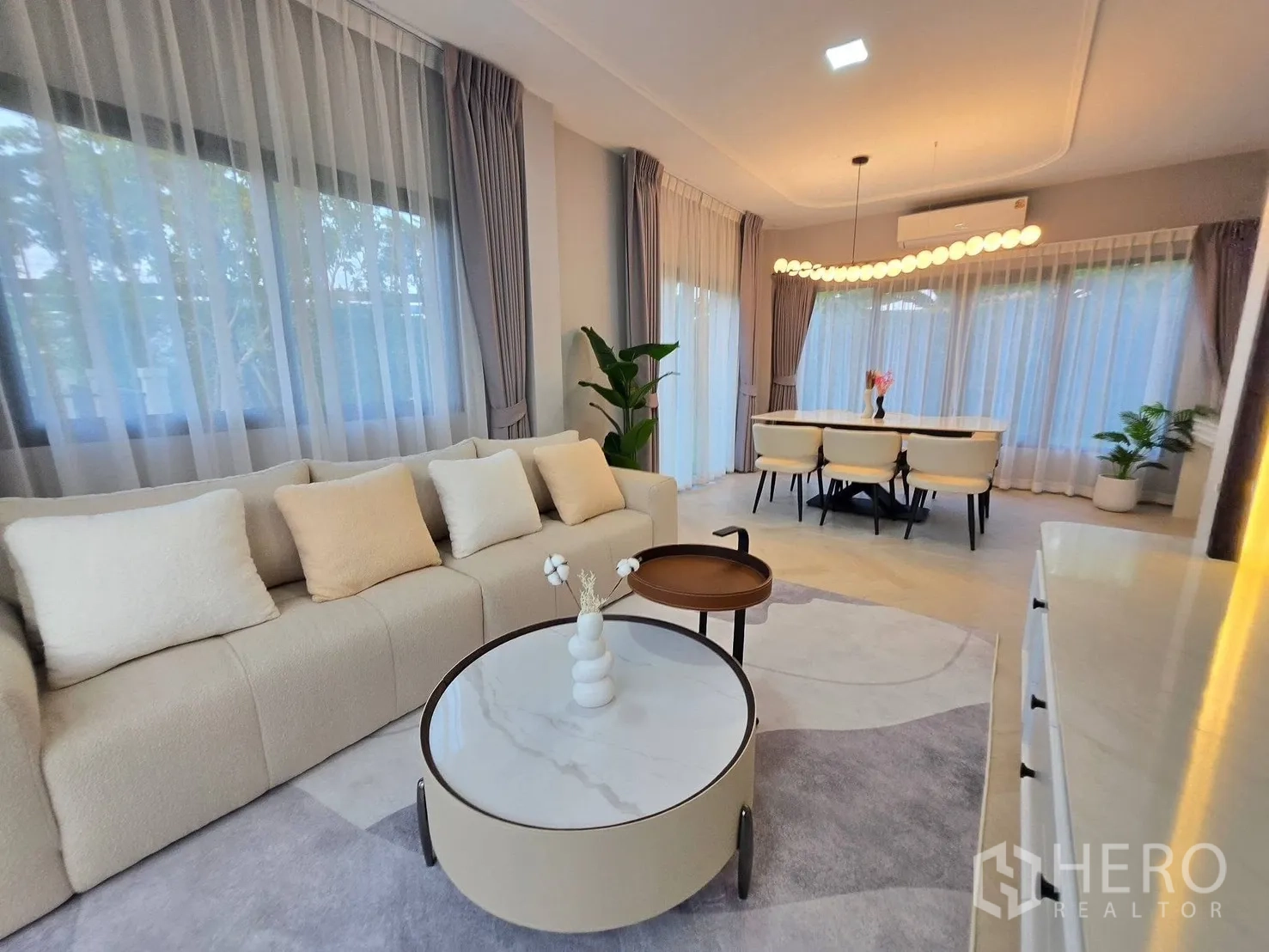 Detached House for rent or sale in Bang Phli, Samut Prakan - Open-plan living and dining with plush sofa, round nesting coffee tables, and wide windows.
