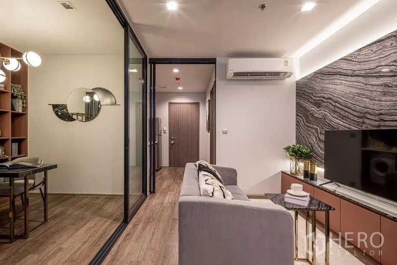 Condominium for sale in Chatuchak, Bangkok - Cozy living area with sofa, TV, and a separate workspace behind a glass partition.