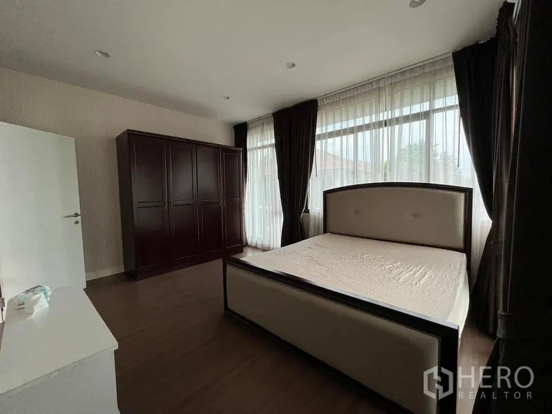 Detached House for rent in Bang Kapi, Bangkok - Sunlit bedroom with large windows, curtains and wooden wardrobe