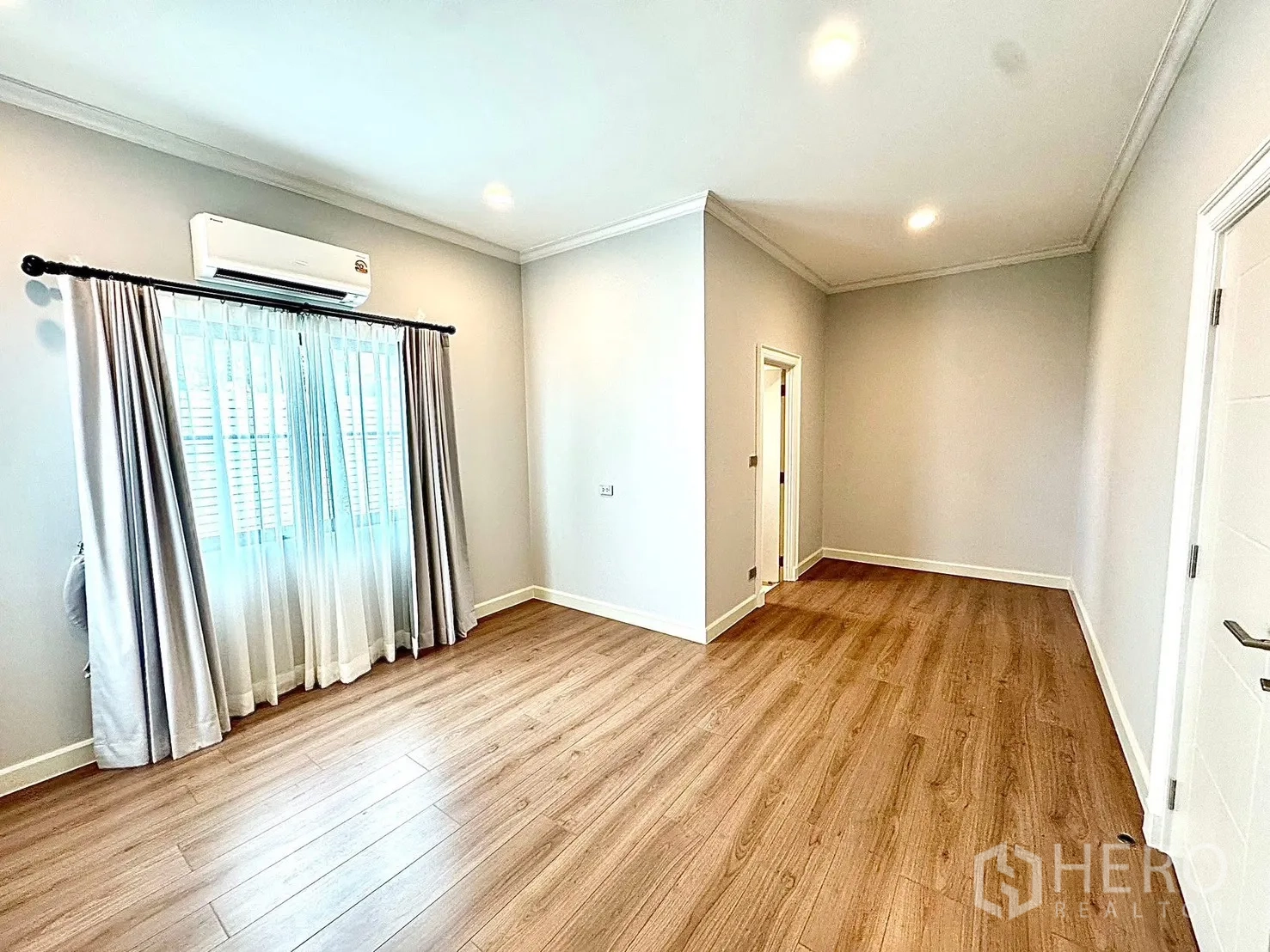 Detached House for rent in Bang Phli, Samut Prakan - Spacious bedroom with wood floors, soft gray walls and a doorway to an en-suite bathroom.