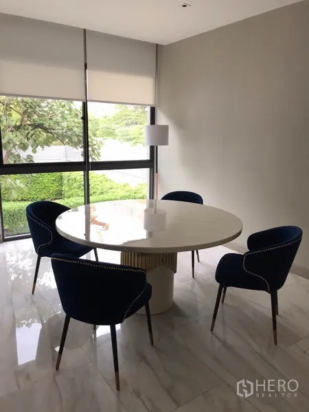 บ้าน ให้เช่าในWatthana, Bangkok - มุมทานอาหารสว่าง โต๊ะกลมสีขาว เก้าอี้สีน้ำเงินสี่ตัว ข้างหน้าต่างบานใหญ่พร้อมมู่ลี่ และพื้นหินอ่อน