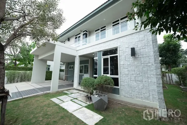 Detached House for rent or sale in Prawet, Bangkok - Front corner showing stone-clad exterior wall, large windows and a small lawn.