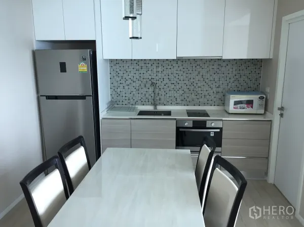 公寓 出租在Watthana, Bangkok - 现代化厨房配餐桌、嵌入式烤箱、炉灶、冰箱与马赛克背墙。