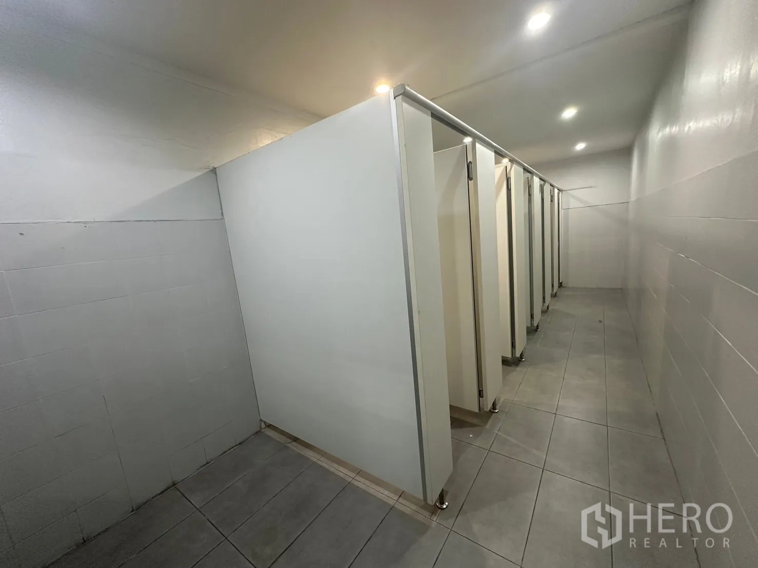 Warehouse for rent in Din Daeng, Bangkok - Row of clean restroom stalls with tiled floor and partitions.