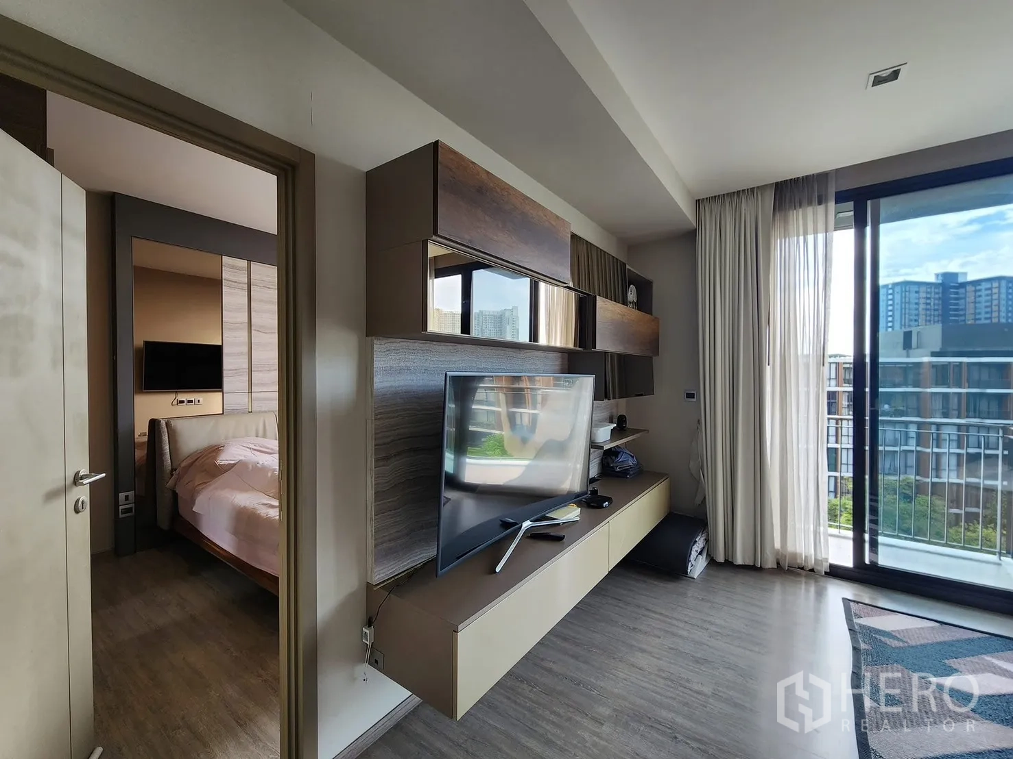 Condominium for rent in Watthana, Bangkok - Living room media wall and doorway to the bedroom, with large sliding doors to the balcony.