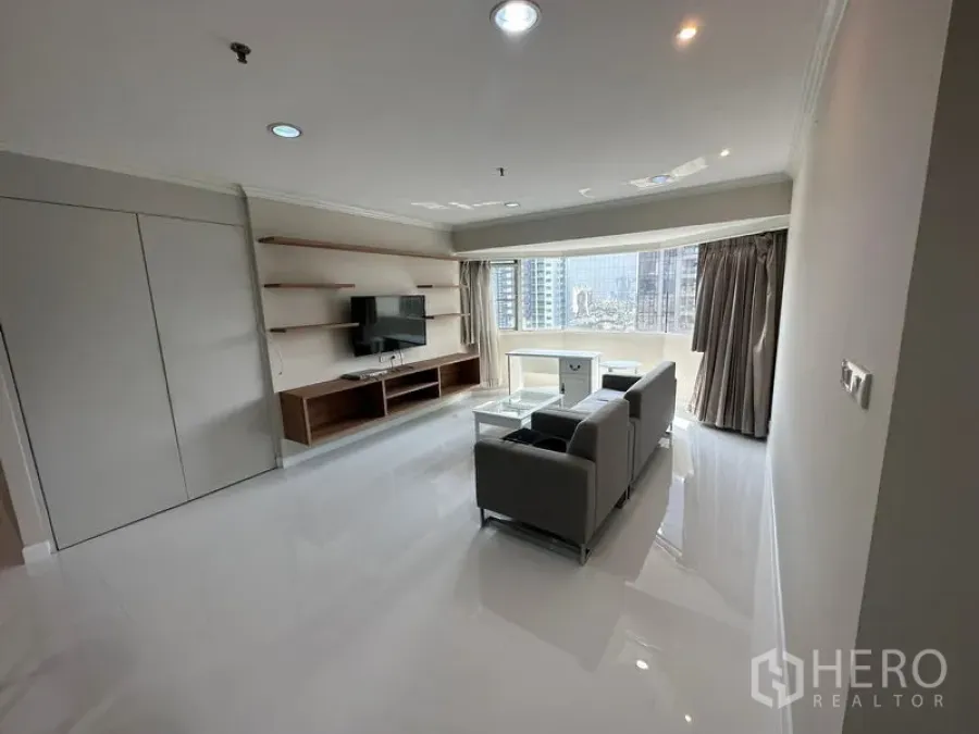 คอนโด ให้เช่าในWatthana, Bangkok - ห้องนั่งเล่นสว่าง โซฟา ผนังติดทีวี พร้อมชั้นวาง และหน้าต่างบานโค้งมองเห็นสกายไลน์กรุงเทพฯ