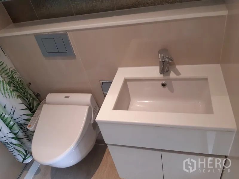 Condominium for rent in Watthana, Bangkok - Close-up of white vanity basin and bidet toilet in a neutral-toned bathroom.
