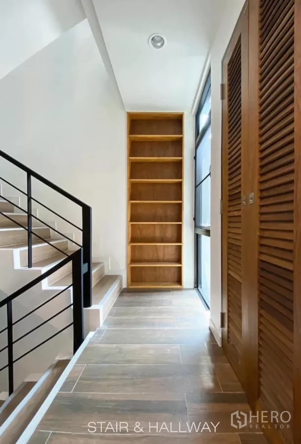 Detached House for rent in Huai Khwang, Bangkok - Upper hallway with staircase, wooden louvered closets and open shelving by a tall window.