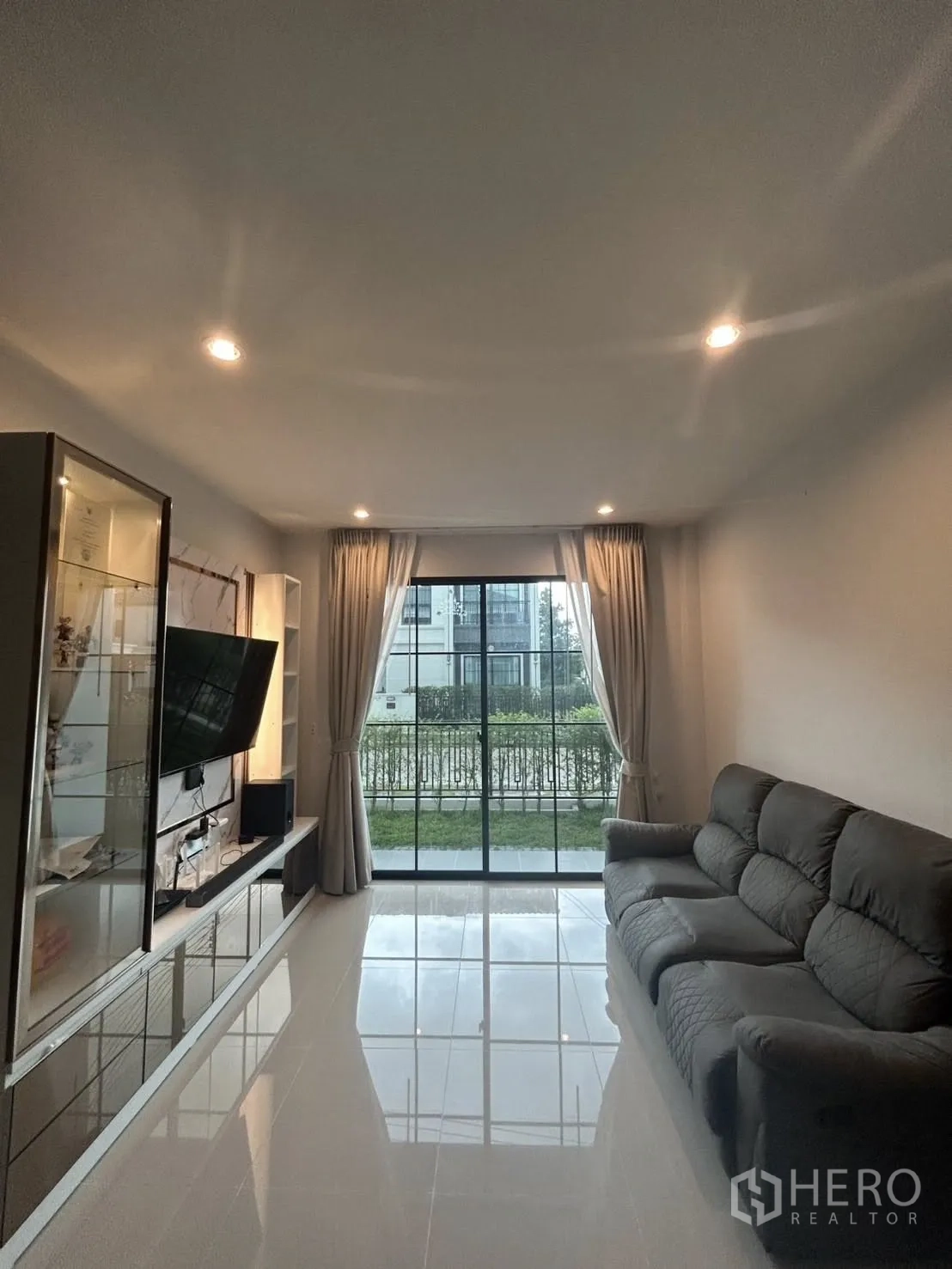 Detached House for rent in Khlong Sam Wa, Bangkok - Bright living room with glossy tile floors, built-in TV wall and sliding glass doors to the garden.